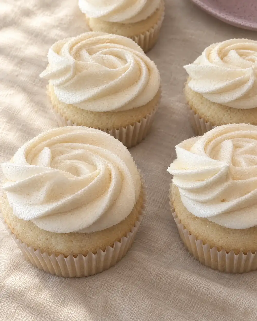 Buttercream cupcakes with swirled rosettes in white liners on cream linen