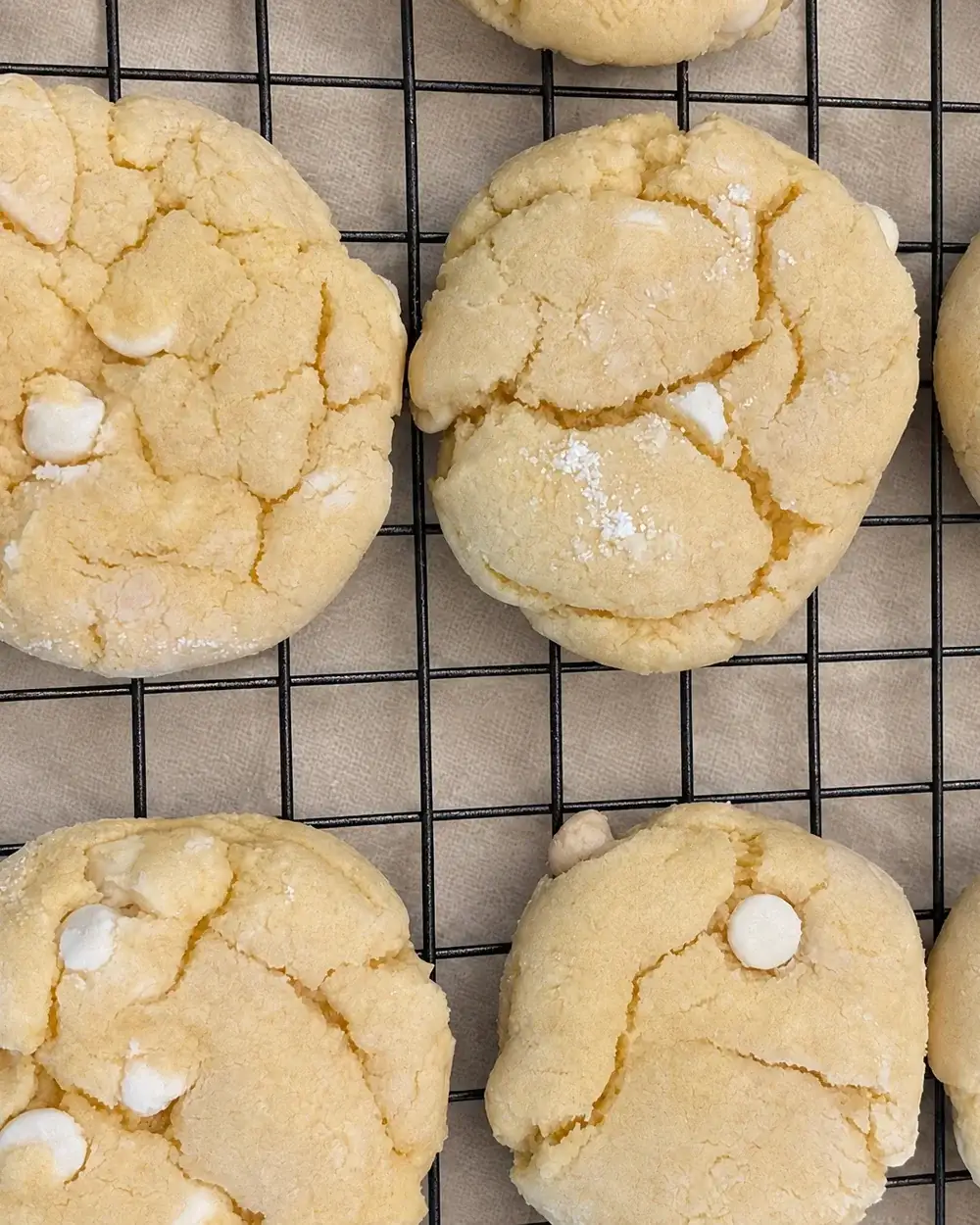 A cooling rack of white chocolate chip cookies set on cream linen