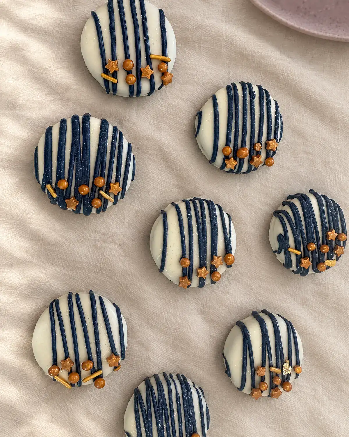 Chocolate-dipped Oreos in navy and white stripes with gold star sprinkles, laid out on cream linen