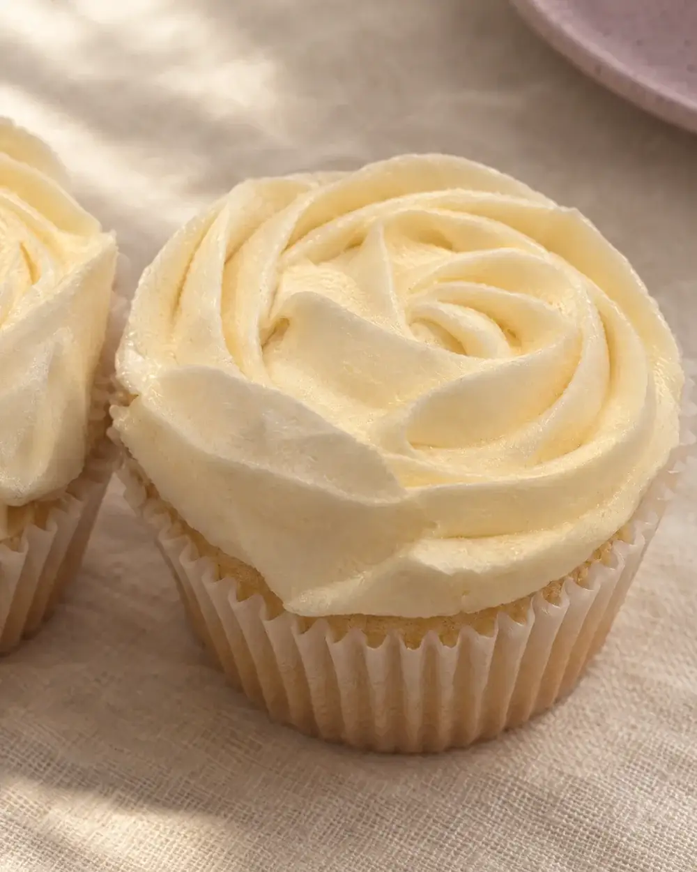 A cupcake piped with a large buttercream rosette, close up on cream linen